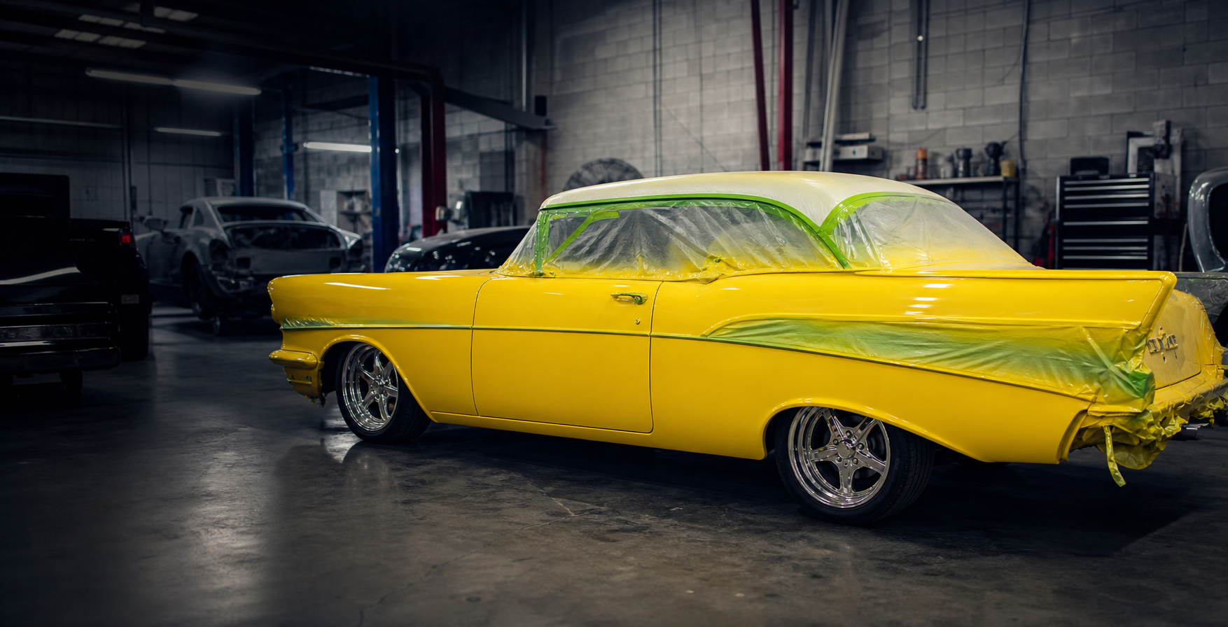 Yellow classic coupe masked for paint inside an active body shop bay